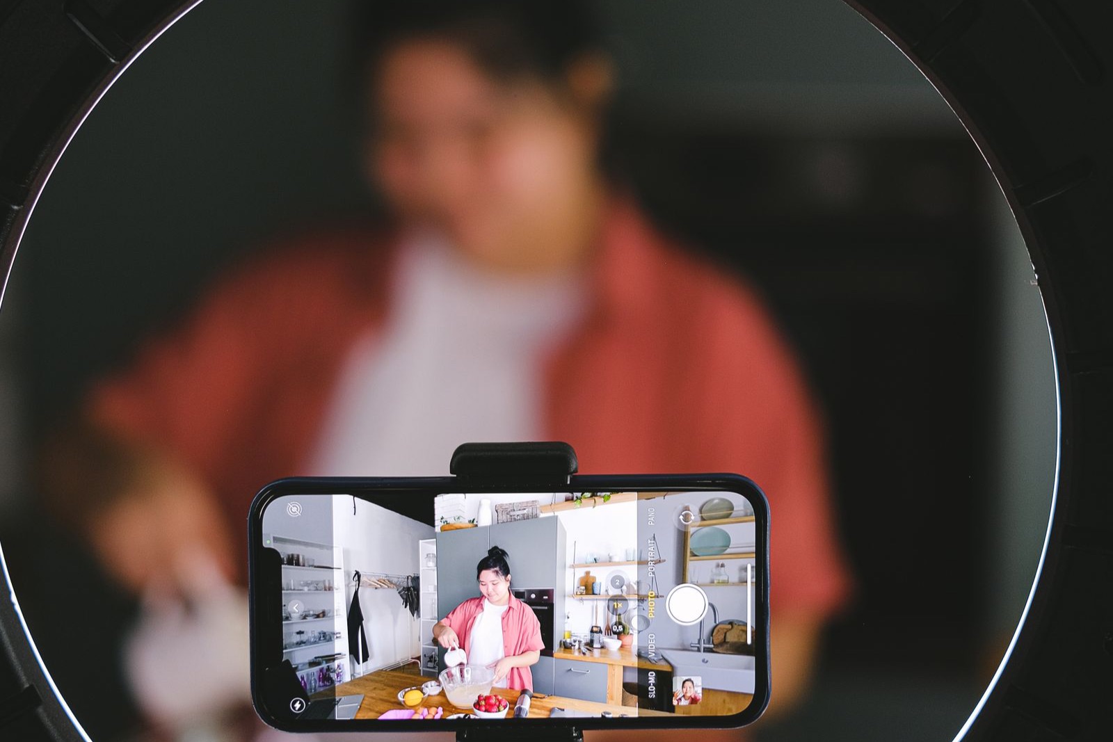 Người nội trợ đứng bếp nấu ăn, phía trước là điện thoại gắn ring light đang quay